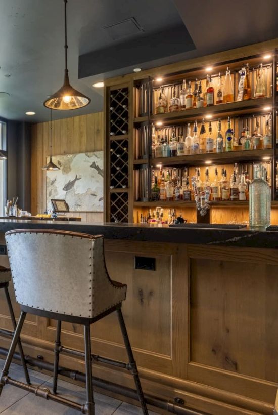A modern mountain bar with shelves of bottles, pendant lights, tall chairs, and a stone wall facing scenic views.