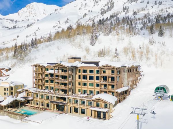 A snowy mountain ski resort with a hotel, heated pool deck, and chairlifts beneath towering white peaks.