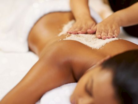 A person&rsquo;s feet and legs being exfoliated with a sandy scrub during a massage.