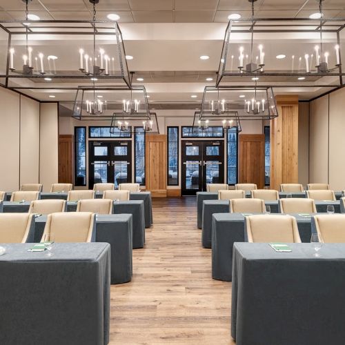 A modern conference room set with gray-covered tables, beige chairs, and hanging chandeliers.