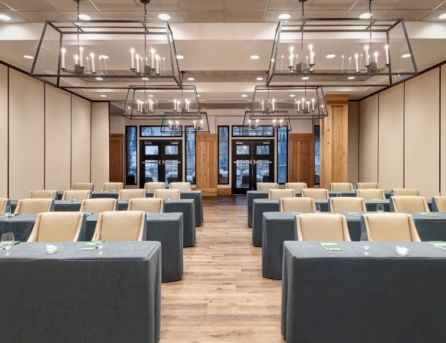 A modern conference room set with gray-covered tables, beige chairs, and hanging chandeliers.