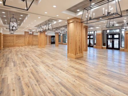 Bright modern event hall with wood-paneled walls, warm hanging chandeliers, and polished wooden floors.