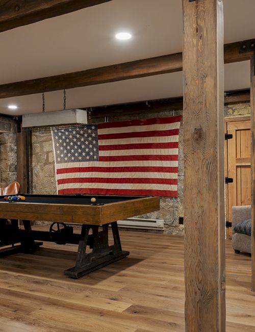 A billiards room with an American flag on the wall, stone-and-wood decor, and seating in the background.