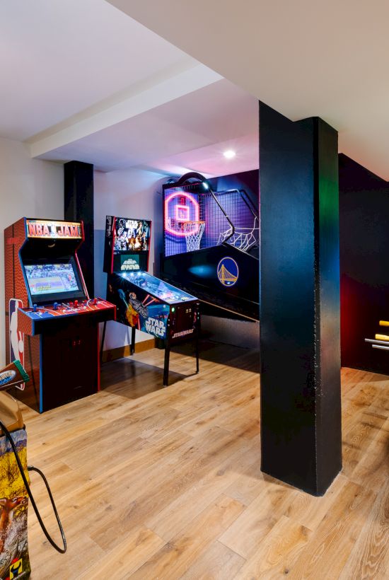Bright arcade room filled with neon video games, foosball and air-hockey tables, and a glowing basketball hoop area.