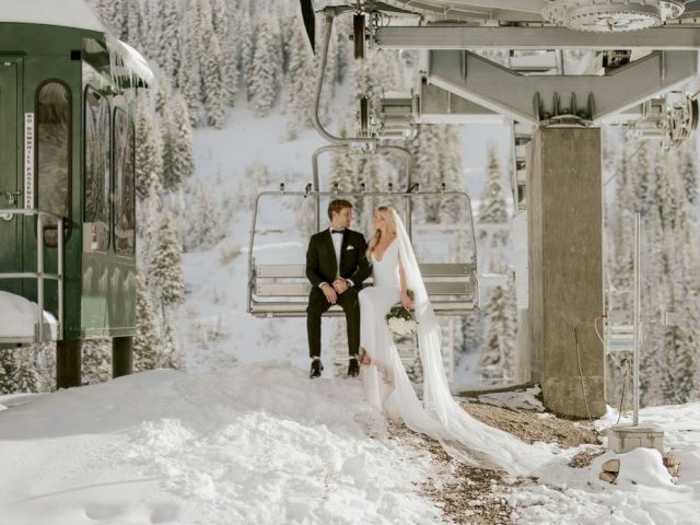 A bride and groom in wedding attire pose inside a snowy industrial setting surrounded by machinery.
