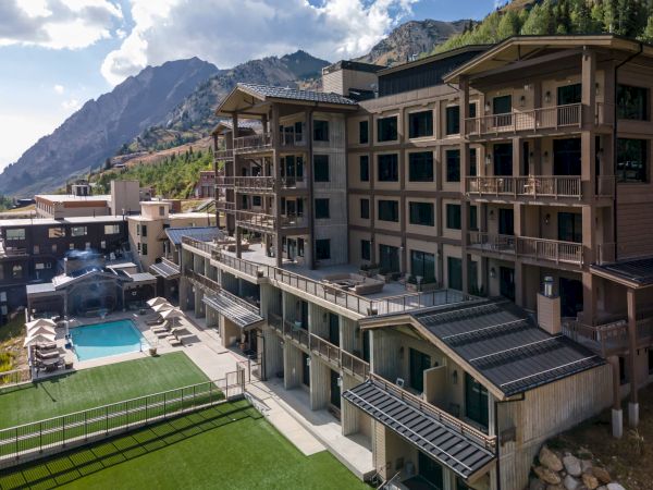 A modern mountain hotel with balconies, a rooftop pool, and green hills under dramatic clouds.