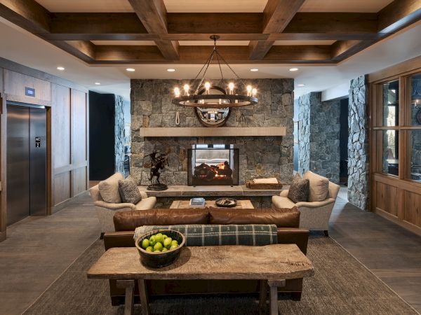 A cozy lodge living room with a stone fireplace, warm chandelier, plush sofas, and a coffee table with green grapes.