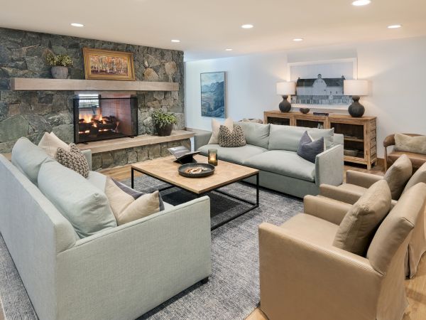 Cozy living room with a stone fireplace, light couches, a wooden coffee table, and wall art under warm ceiling lights.