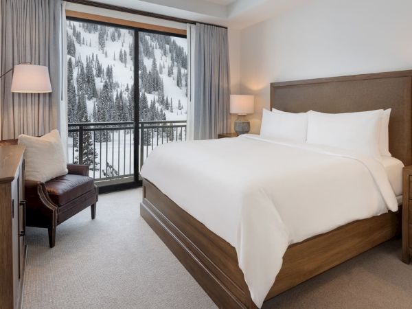 A cozy hotel bedroom with a large bed and mountain view through a snowy window, warm lamps lighting the room.