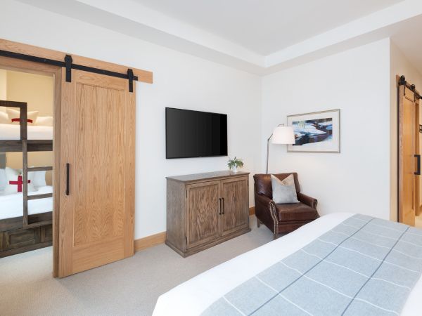 A modern bedroom with a wooden door, TV on a cabinet, a lamp, framed picture, and a brown armchair.