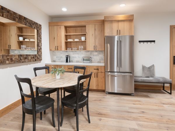 A modern kitchen and dining area with wooden cabinets, a stainless fridge, coffee machine, and a round table with chairs and a bench.
