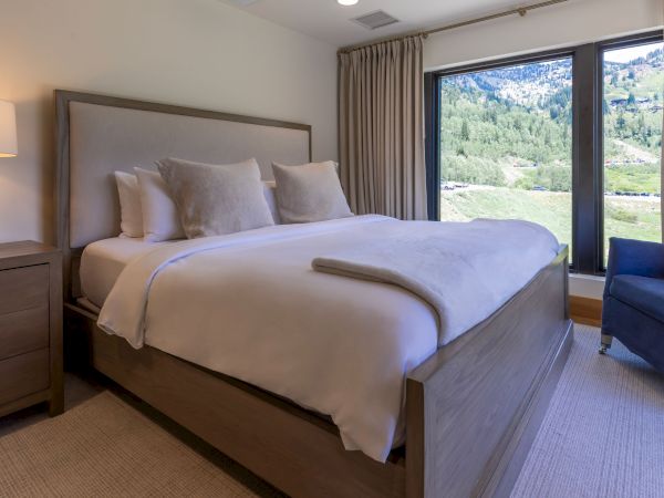 A cozy hotel bedroom with a made bed and pillows, plus large windows showing a lush mountain valley outside.