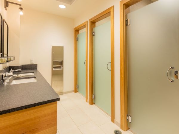 A modern bathroom with a granite double-sink vanity, mirrors, tiled floor, and wood-framed doors.