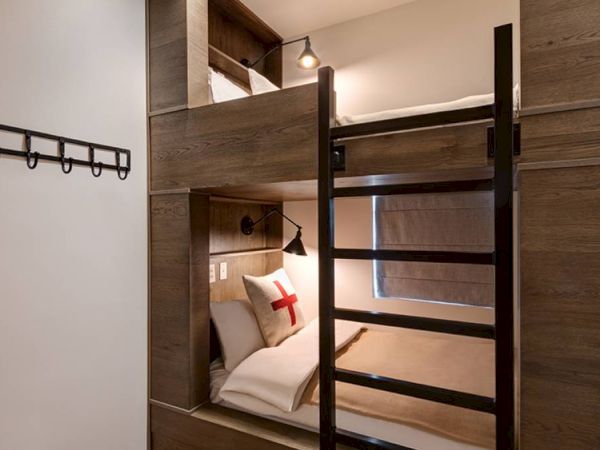 Modern built-in bunk bed in a wooden alcove, with warm lights and a pillow featuring a red cross.
