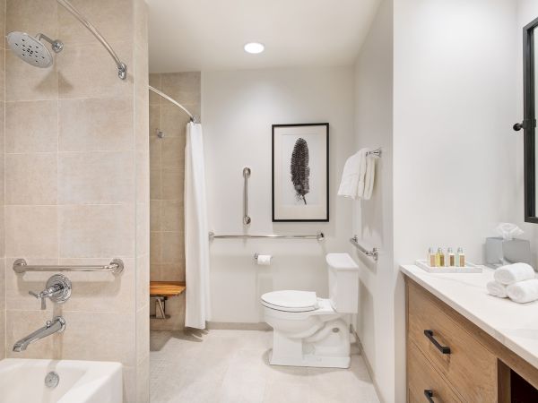 A modern bathroom with a glass shower, toilet, sink counter with towels and toiletries, and framed wall art.