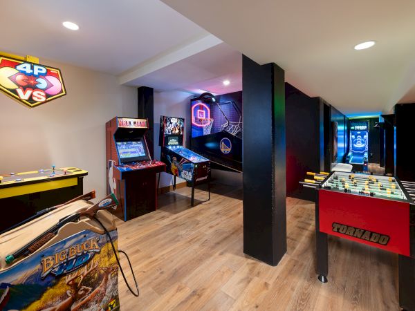 A bright arcade room with foosball and air-hockey tables, plus glowing game cabinets and basketball hoop machines.
