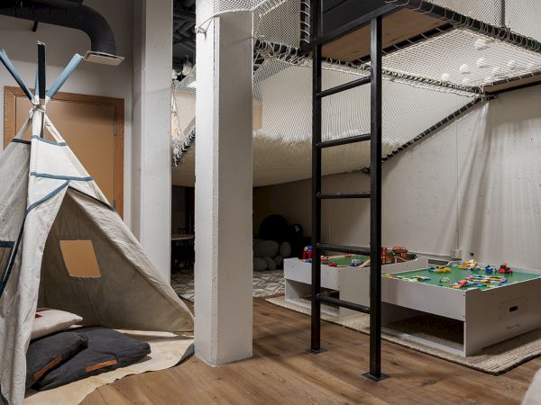 An indoor playroom with a canvas teepee, a netted climbing structure, and a foosball-style toy table and building blocks.