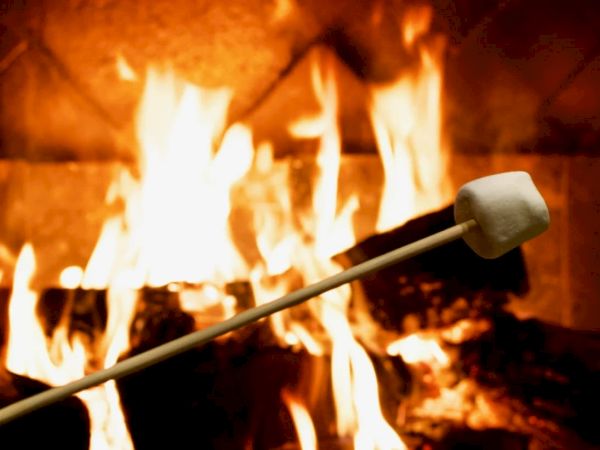 A large fireplace blaze burns hot as a long poker holds a log in place, glowing orange.