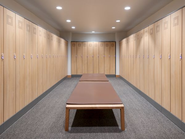 A hallway lined with wooden storage lockers, bright ceiling lights, and a padded exercise mat on a bench-like table.