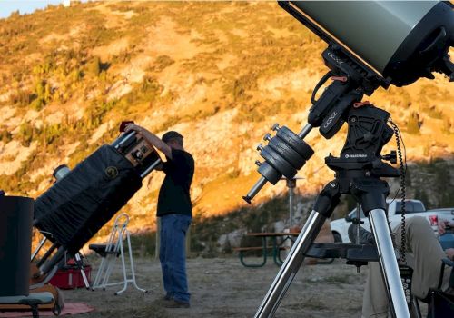 A group sets up and adjusts a large telescope outdoors on a hillside at sunset.