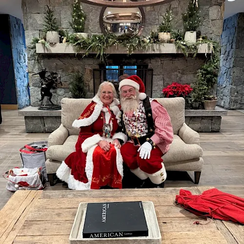 An older couple dressed for Christmas pose on a couch with garland and a coffee-table book titled &ldquo;American Cowboy.&rdquo;