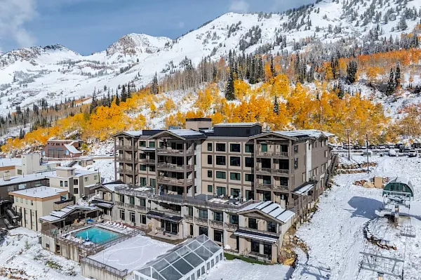 A snowy mountain resort with a multi-story hotel, outdoor pool, and autumn-gold trees under alpine peaks.