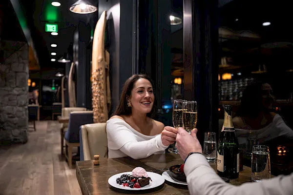 In a chic restaurant, a woman toasts with champagne while enjoying dessert at a table.
