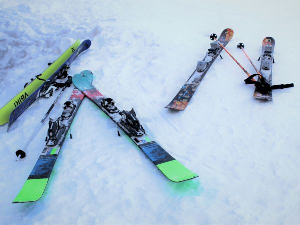 Snow-covered scene with several ski boards laid out, showing bindings and poles on a flat ski slope.
