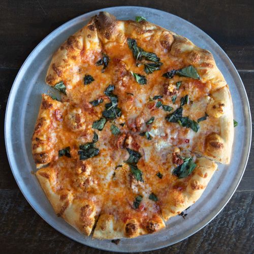 A cheese pizza with tomato sauce, browned crust, and scattered spinach leaves on a round metal tray.