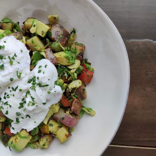 A plate of breakfast with poached eggs over chopped roasted vegetables and herbs.