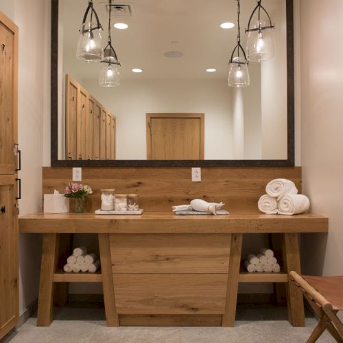 Stylish bathroom with wood vanity, large mirror, hanging glass pendant lights, folded towels, and a small ladder.