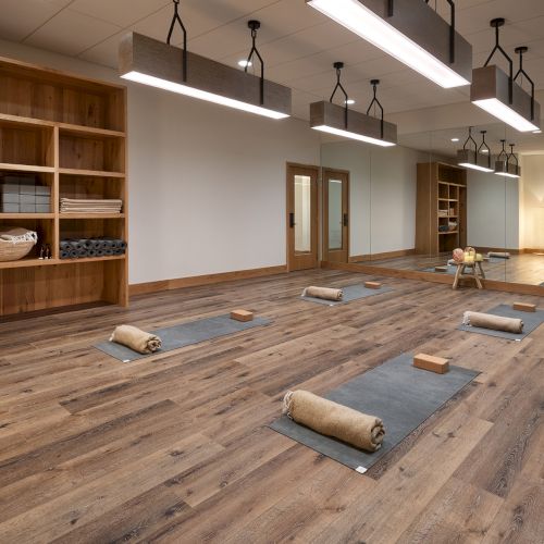 Bright yoga studio: wooden floors, mats, blocks, rolled towels, mirrored wall, storage shelves, and hanging pendant lights.
