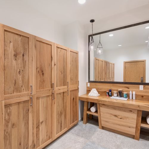 Bright bathroom with rustic wooden cabinets, a large mirror, a vanity countertop with toiletries, towels, and hanging glass light fixtures.