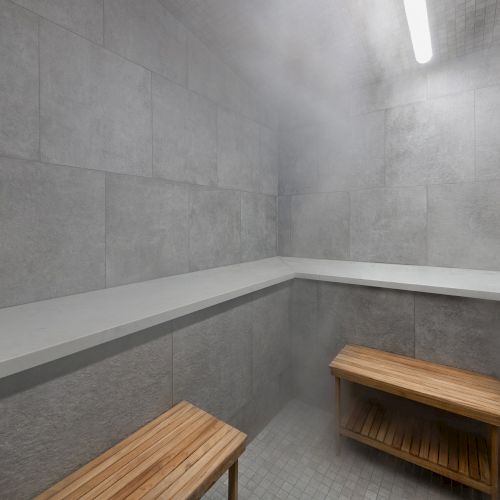 Gray tiled sauna/steam room corner with wooden benches and a bright ceiling light.