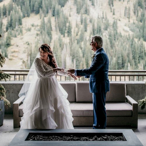 A bride and groom exchange rings on a terrace with pine decor and snowy mountains in the background, in a wedding ceremony.