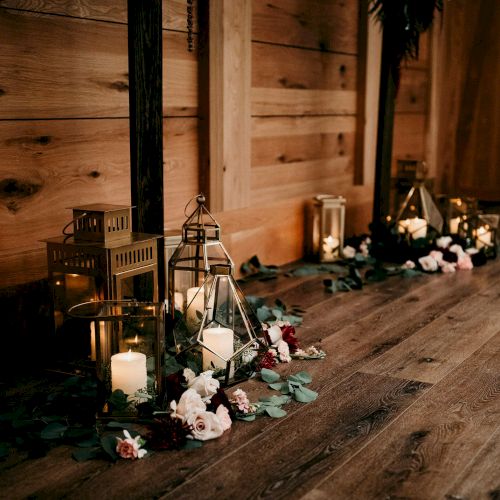 A cozy indoor setup with lit lanterns and candles, plus scattered flowers on a wooden floor near a doorway.