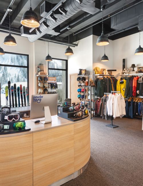 A bright ski shop filled with skis, goggles, jackets, and colorful winter gear under hanging lights.