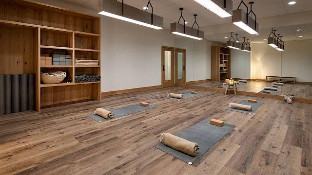 A bright yoga studio with wooden shelves, floor yoga mats with blocks, and hanging pendant lights.
