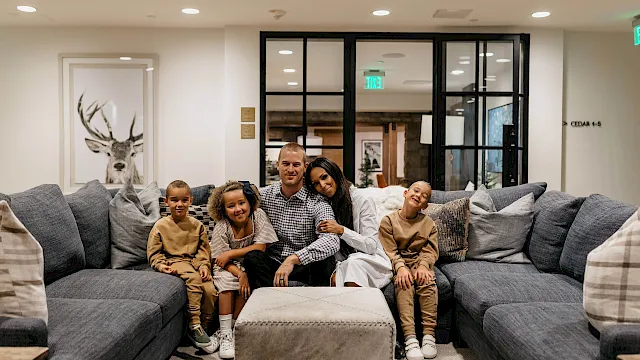 A family of five poses on a gray couch in a bright modern living room, smiling together.