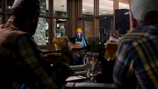 A live acoustic performance in a cozy bar, with a musician singing onstage while guests watch nearby.