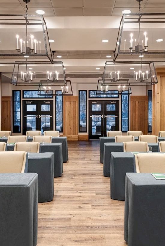 A modern conference room set with gray tables, beige chairs, and hanging candle-style lights under a grid ceiling.